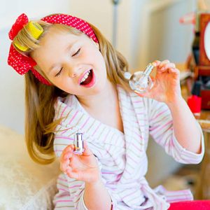 the little girl poses in pin up style in a striped terry dressing gown, in hair curlers and with a red bandage in peas, with a bottle of perfume in hands